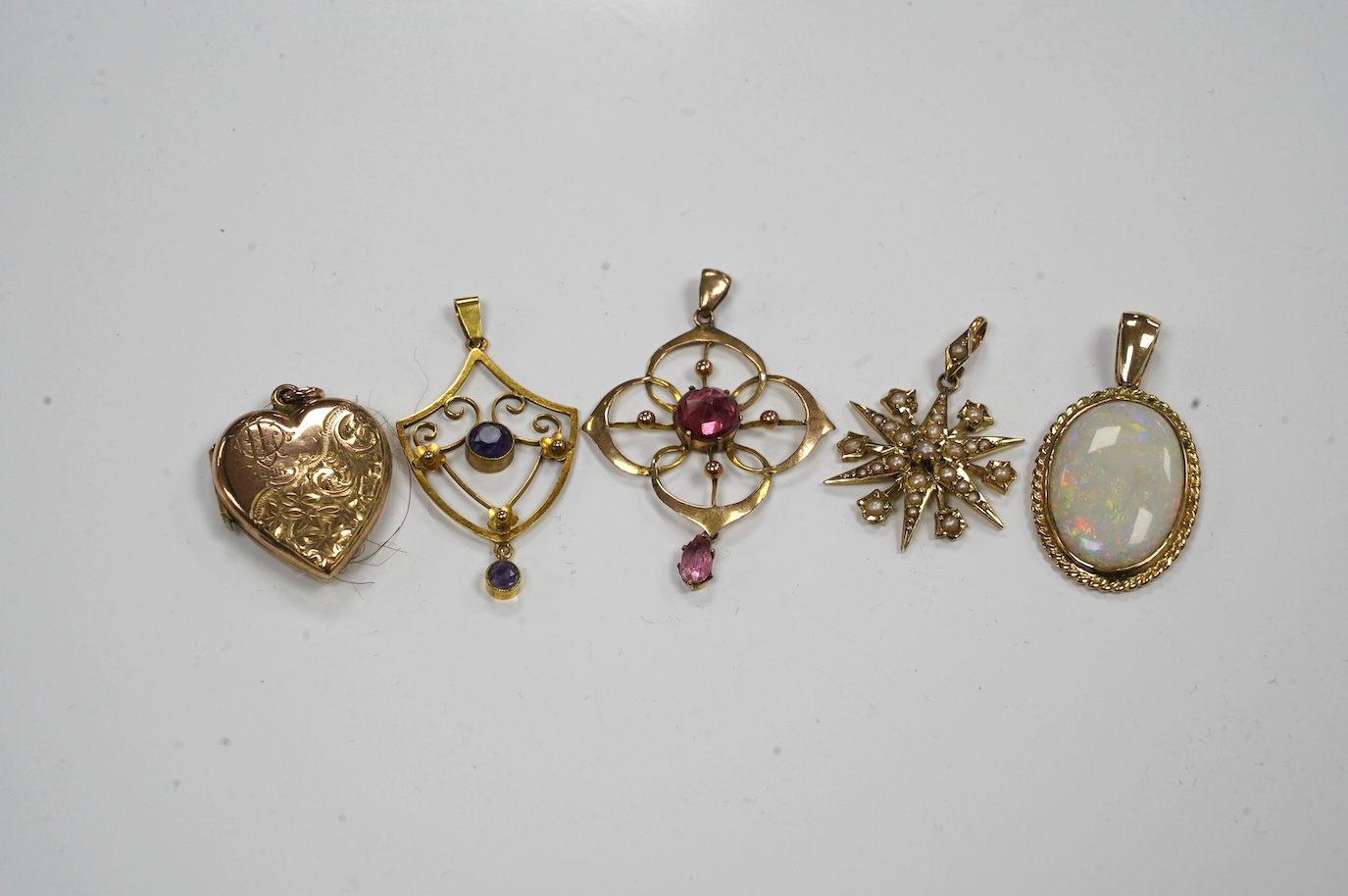 Five assorted gem set pendants including a 9ct and seed pearl star, 20mm, a yellow metal and amethyst set drop, a yellow metal and white opal and an Edwardian yellow metal heart shaped locket. Condition - fair